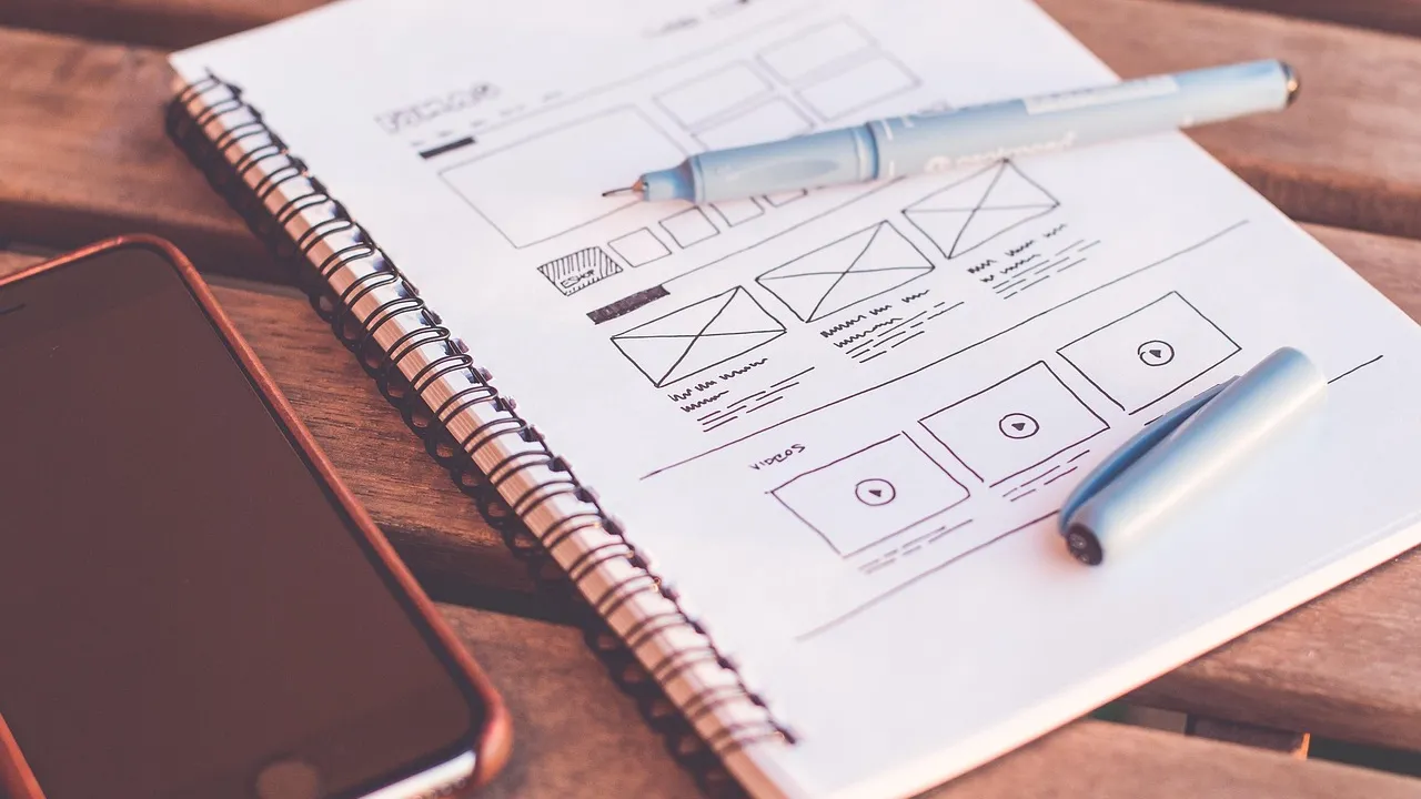 Schetsboek met een getekend ontwerp van een website, met een pen en een smartphone op een houten tafel